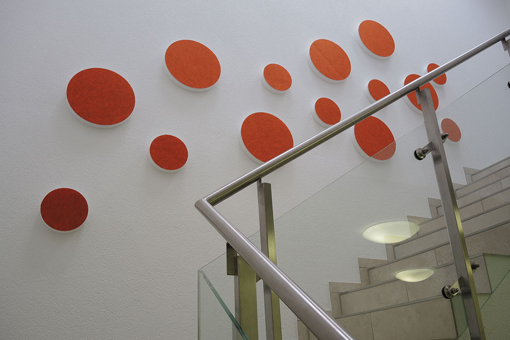 soni ELEMENT CIRCLE 14 sound absorbers in the shape of a circle (soni ELEMENT CIRCLE) in the color orange mounted on a white wall in a modern stairwell.