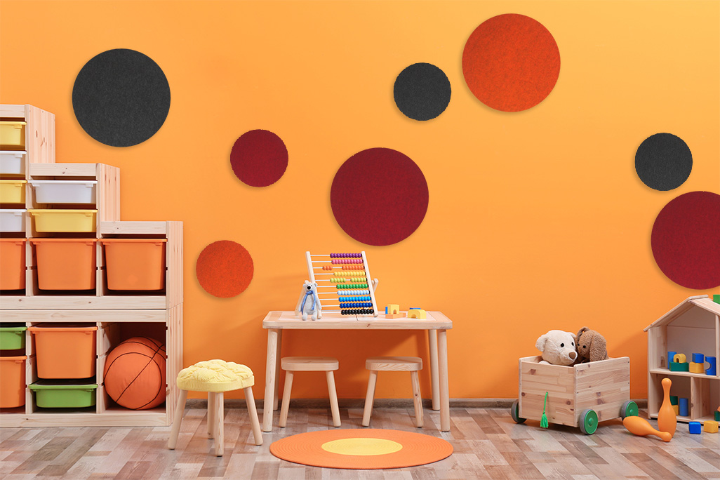 soni ELEMENT CIRCLE 8 colored sound absorbers in the shape of a circle (soni ELEMENT CIRCLE) in two different sizes on an orange wall in a children's room with toys and children's furniture.