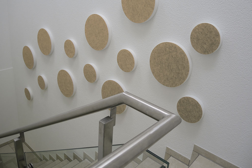 soni ELEMENT CIRCLE 14 sound absorbers in the shape of a circle (soni ELEMENT CIRCLE) in the color beige mounted on a white wall in a modern stairwell.