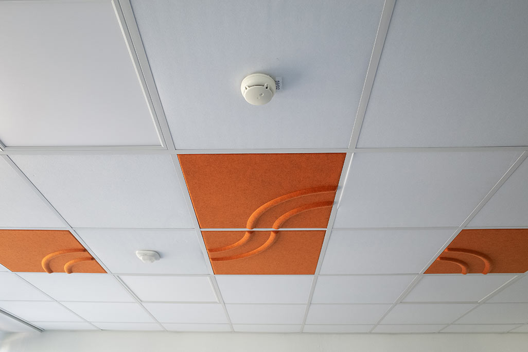 Section of a standard grid ceiling with inlaid soni COMFORT SD acoustic absorbers in white and soni COLOR Design in orange.