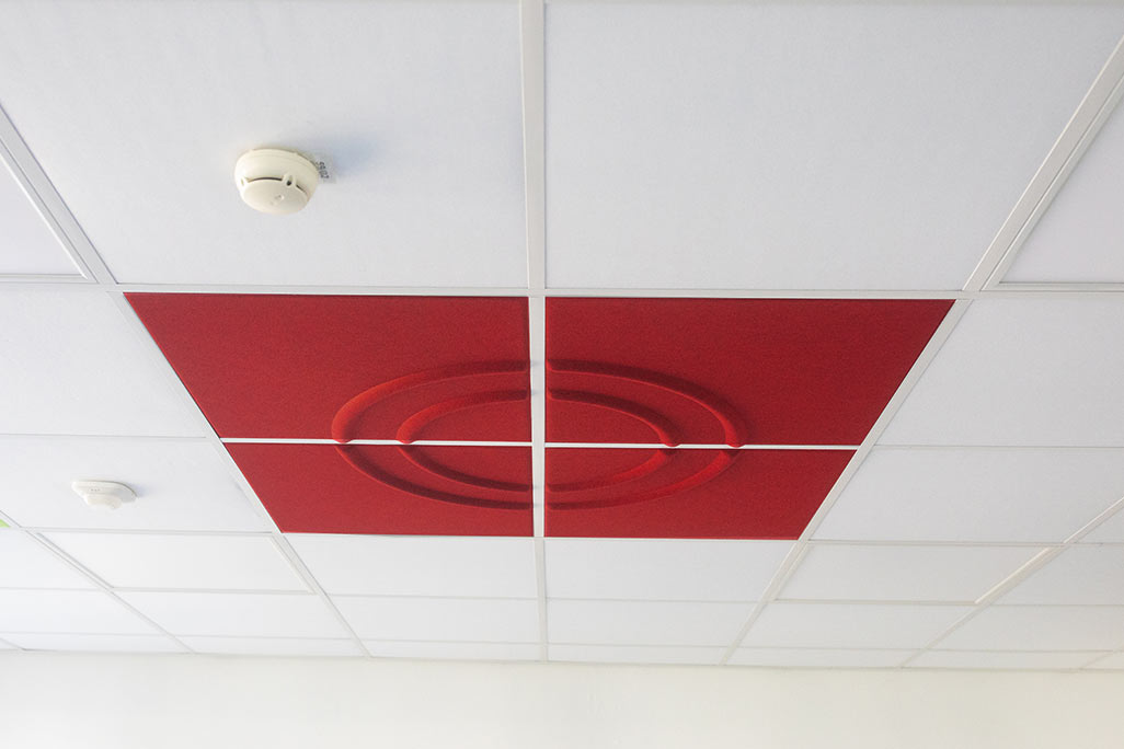 Section of a standard grid ceiling with inlaid soni COMFORT SD acoustic absorbers in white and soni COLOR Design in red.