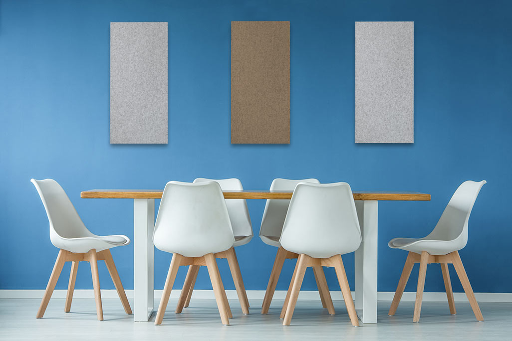 Dining table with white chairs and a blue wall with three rectangular acoustic elements in beige and greige.