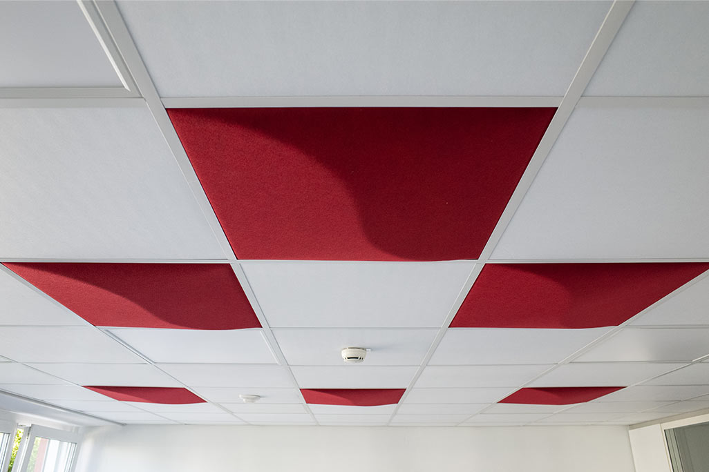 Section of a standard grid ceiling with inlaid soni COMFORT SD acoustic absorbers in white and soni COLOR Design in light red.