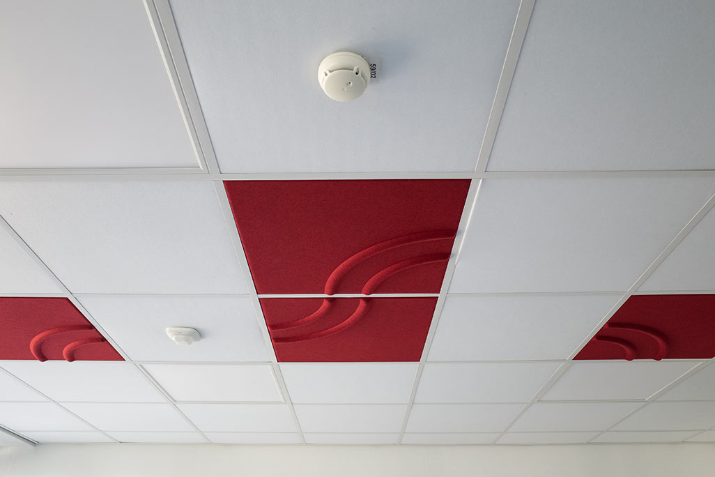 Section of a standard grid ceiling with inlaid soni COMFORT SD acoustic absorbers in white and soni COLOR Design in red.