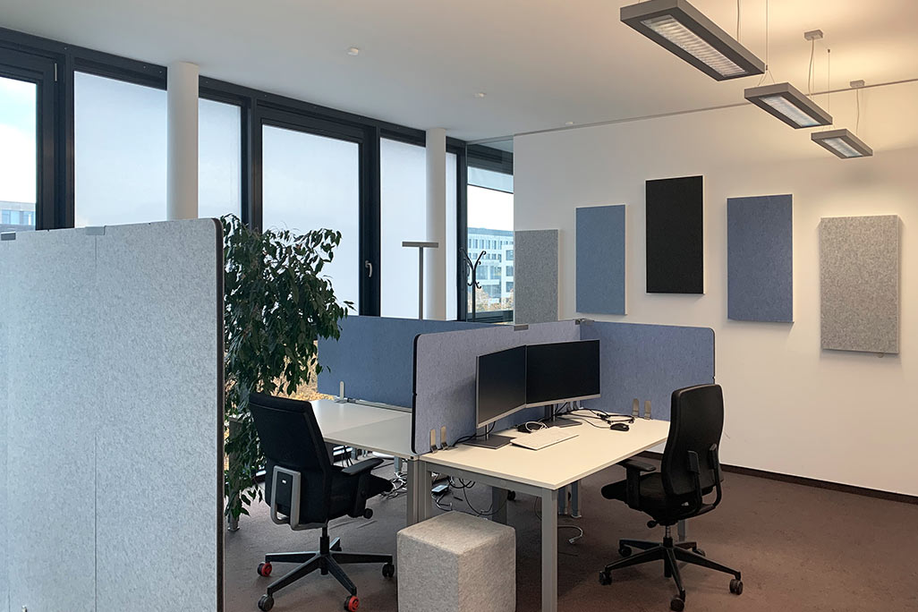 Modern office with large windows, desk, acoustic absorbers on the wall and partitions on the desks